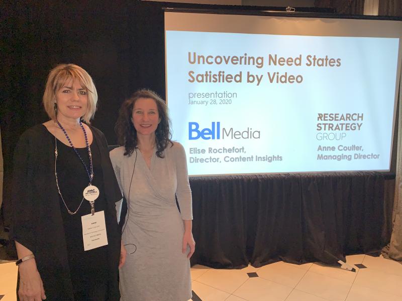 Two females standing to the left of a projector screen with "Uncovering Needs States Statisfied by Video" at a conference