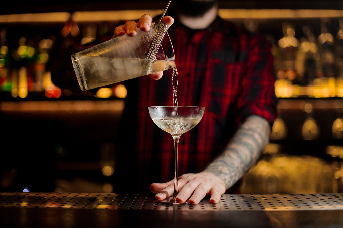 Bartender pouring alcoholic cocktail into an elegant glass on the bar counter against the lights
