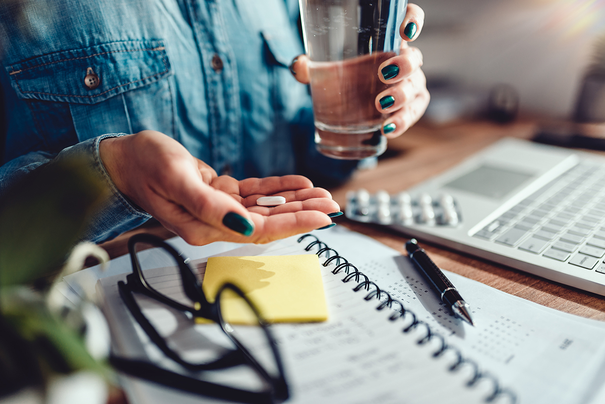 Woman wearing denim shirt sitting by the desk in the office and taking medical pills