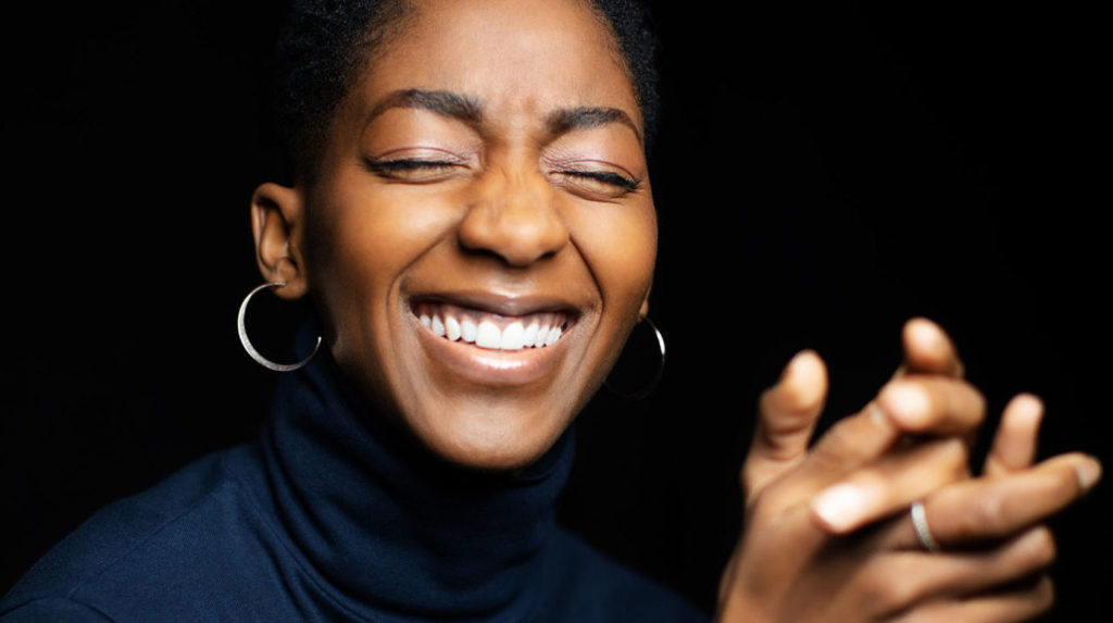 close up of female laughing with eyes closed, wearing navy turtleneck, clasping hands together