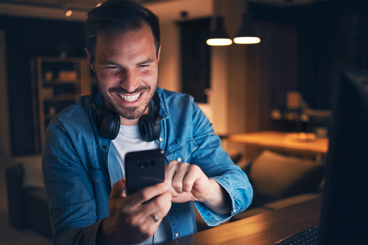 Excited man sitting in his home office, looking at his cellphone with a big smile on face