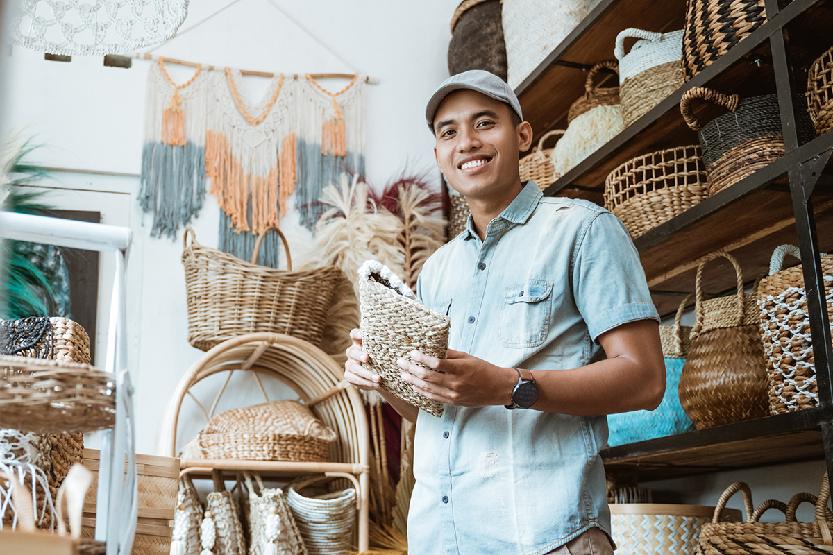 young entrepreneur smiles while holding a wicker wallet while standing in a craft shop