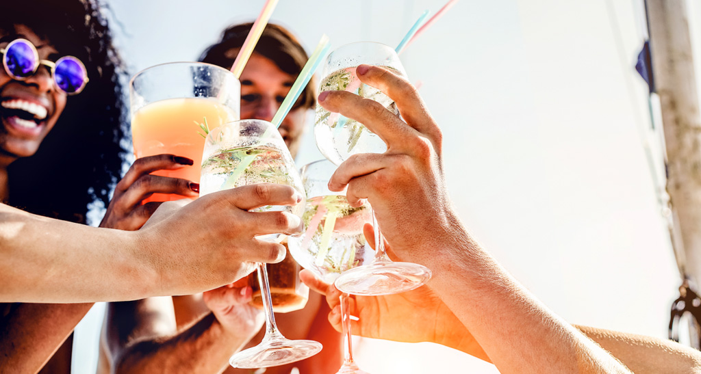 young adults, clinking cocktails together in sunshine