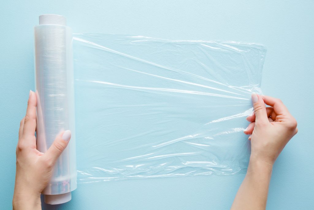 two female hands pulling plastic film wrap across a light blue surface