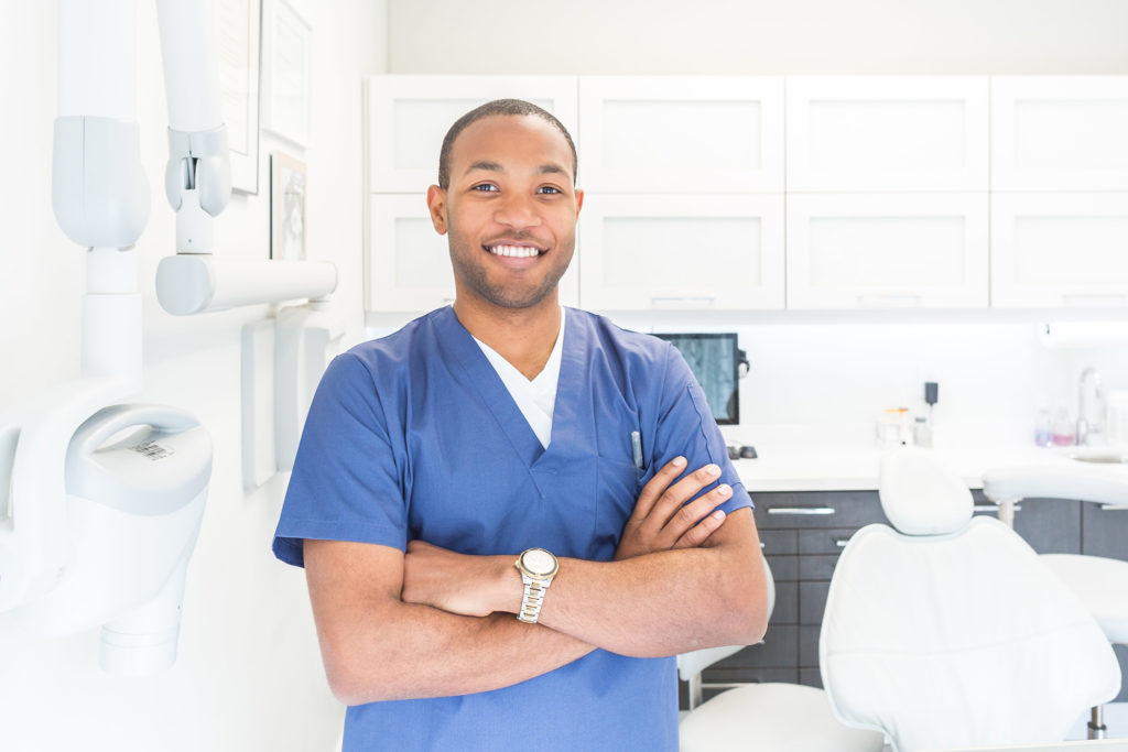 bright white dentist's office with smiling male dentist wearing blue scrubs